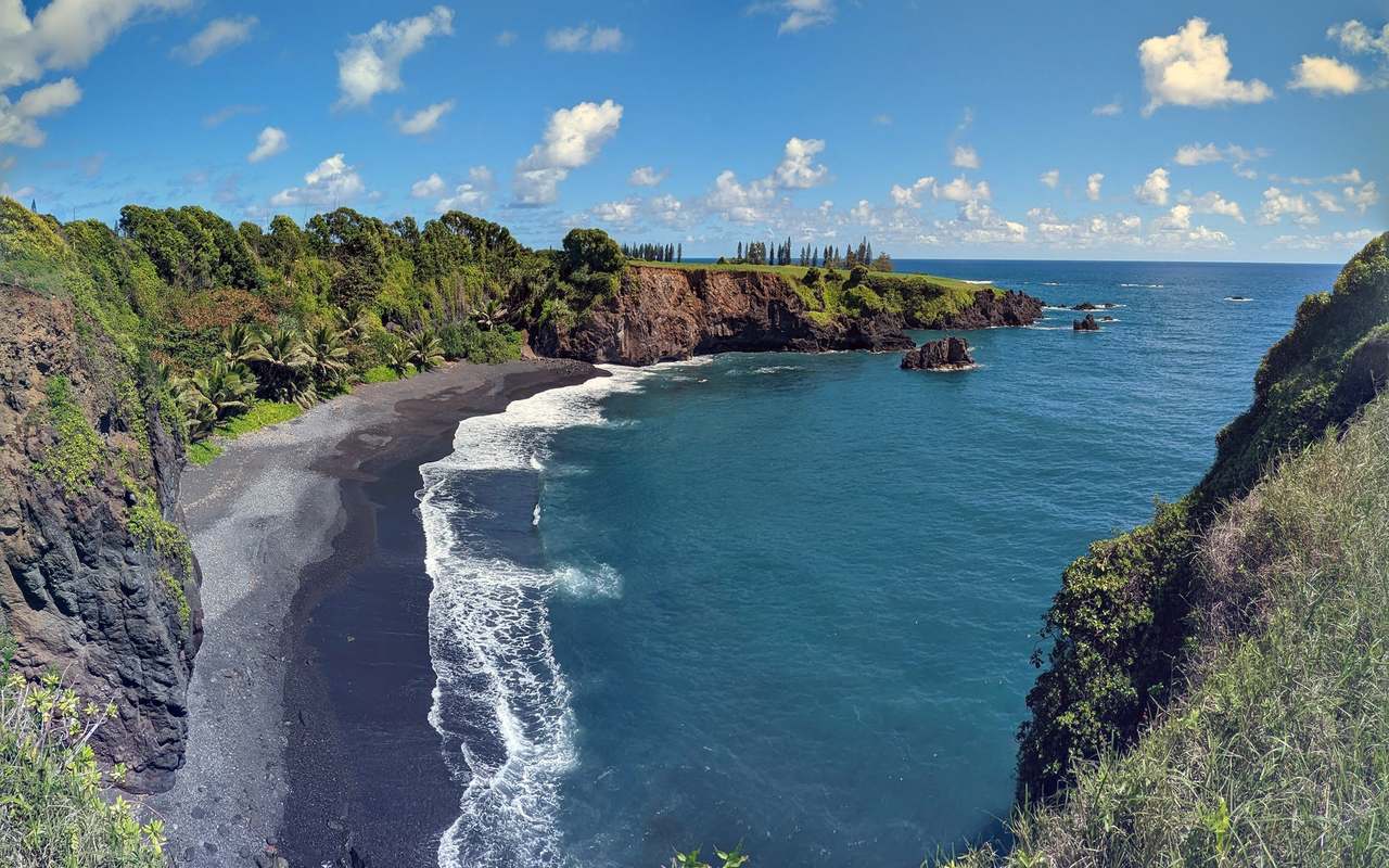 A black-sand cove below a basalt cliff, with a lava headland and open ocean beyond.